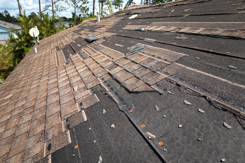 Wind damaged house roof with missing asphalt shingles after hurricane Ian in Florida.