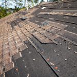Wind damaged house roof with missing asphalt shingles after hurricane Ian in Florida.